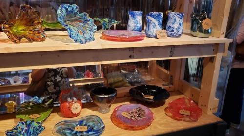 A display of colorful glass art pieces, including bowls and vases, arranged on wooden shelves.