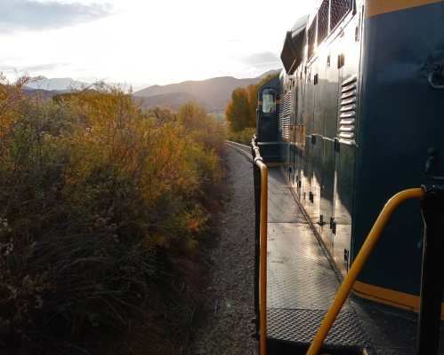 A train engine on a winding track surrounded by autumn foliage and mountains under a sunset sky.
