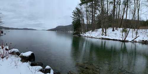 A serene winter landscape featuring a calm lake surrounded by snow-covered trees and rocky shores.