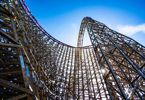 A close-up view of a wooden roller coaster's steep curve against a bright blue sky.