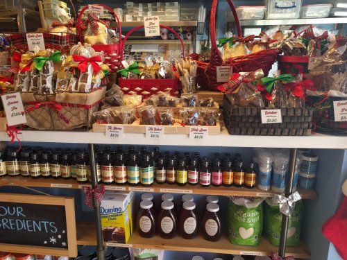 A display of assorted treats in baskets, with jars of ingredients and prices on a shelf in a cozy shop.