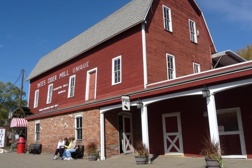 A red barn-style building with a sign reading "Mates Diver Mill Unique," featuring benches and a clear blue sky.