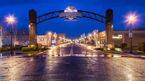 A nighttime view of a downtown archway with lights reflecting on a wet street.