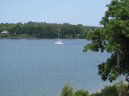 A serene lake scene with a sailboat on the water, surrounded by lush green trees and a clear blue sky.