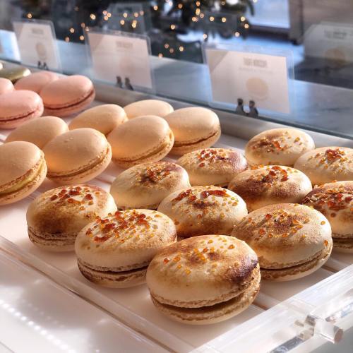 A display of colorful macarons in various flavors, with a snowy backdrop visible through the window.