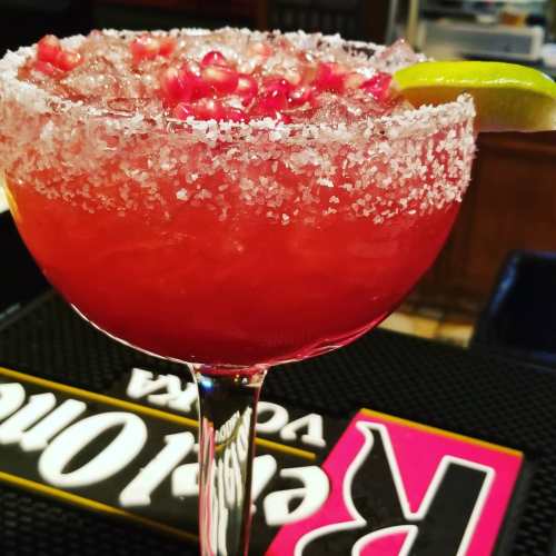 A vibrant red cocktail with a salted rim, garnished with a lime slice, served in a large glass.