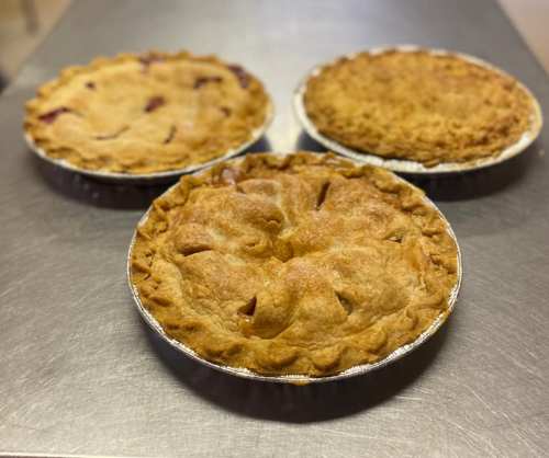 Three freshly baked pies on a metal surface, featuring golden-brown crusts and varying fillings.