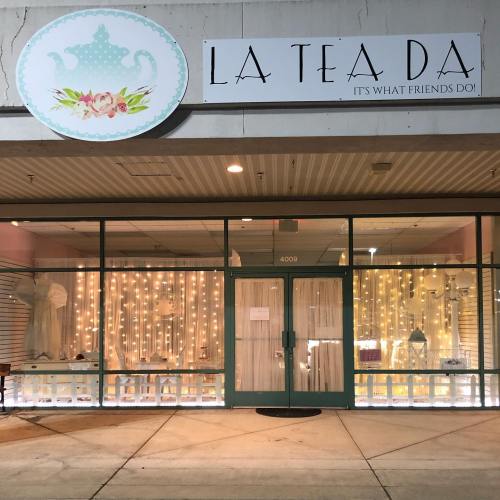 A storefront with a sign reading "LA TEA DA" and decorative lights in the window, creating a cozy atmosphere.
