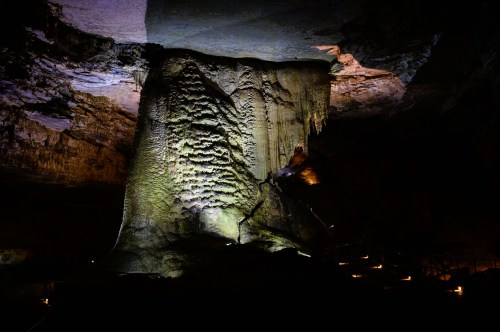 A dimly lit cave interior featuring a large, illuminated rock formation with textured surfaces and colorful lighting.