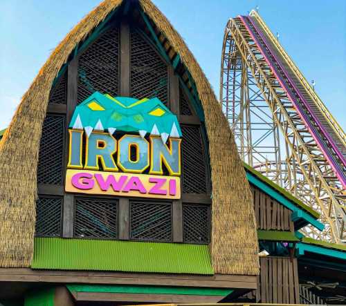 Colorful entrance to the Iron Gwazi roller coaster, featuring a thatched roof and a wooden structure.