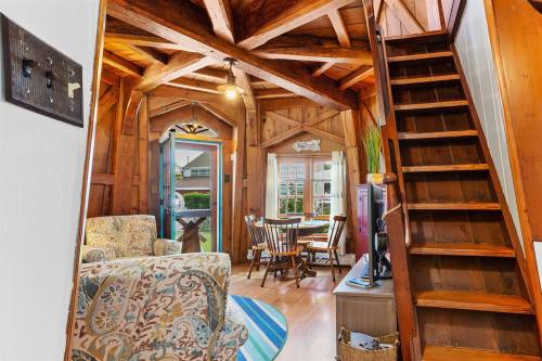 Cozy wooden interior with a staircase, seating area, and dining space, featuring rustic beams and warm lighting.