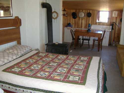 Cozy interior of a rustic room featuring a bed with a quilt, a wood stove, and a dining table with chairs.