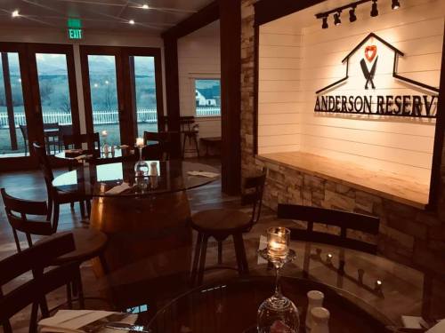 Cozy restaurant interior with wooden tables, chairs, and a lit sign reading "Anderson Reserve" on a stone wall.