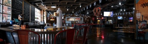 A spacious restaurant interior with a bar, tables, and a staff member at the counter, featuring a lively atmosphere.