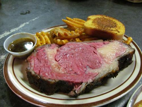 A plate featuring a large slice of prime rib, waffle fries, toast, and a small bowl of dipping sauce.