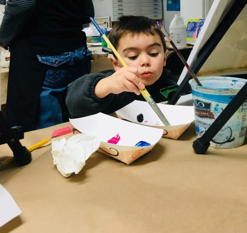 A young child focused on painting, holding a brush over a palette with colorful paints.