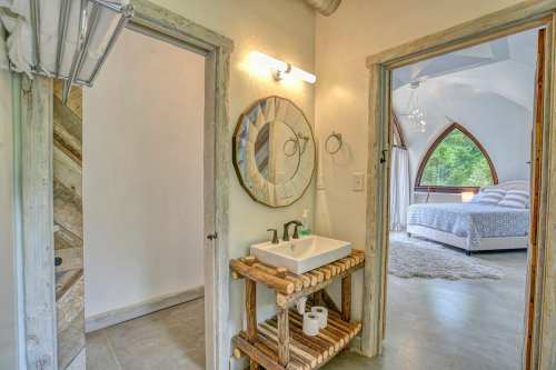 A modern bathroom with a wooden sink stand, leading to a cozy bedroom with arched windows and soft lighting.