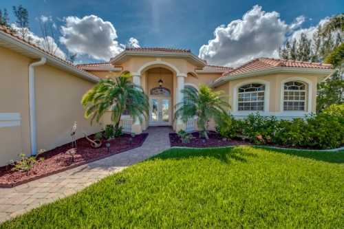 A welcoming entrance to a home with a landscaped yard, palm trees, and a pathway leading to the front door.