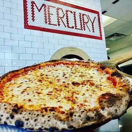 A close-up of a cheese pizza with a thick crust, in front of a wall with the word "MERCURY" made of tiles.