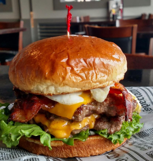 A juicy burger with two patties, melted cheese, bacon, lettuce, and onions, served on a toasted bun with a toothpick.
