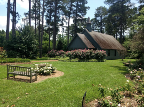 A quaint building surrounded by lush greenery and blooming flowers, with a bench in a garden setting.