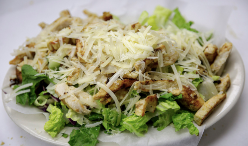 A plate of salad topped with grilled chicken strips and shredded cheese on a bed of fresh lettuce.