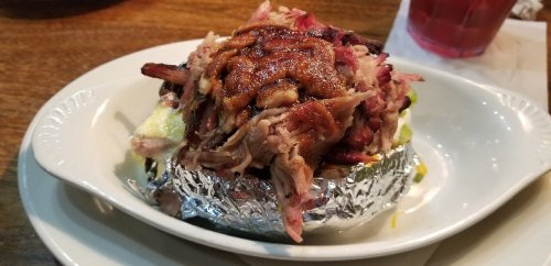 A baked potato topped with pulled pork and barbecue sauce, served on a white plate.