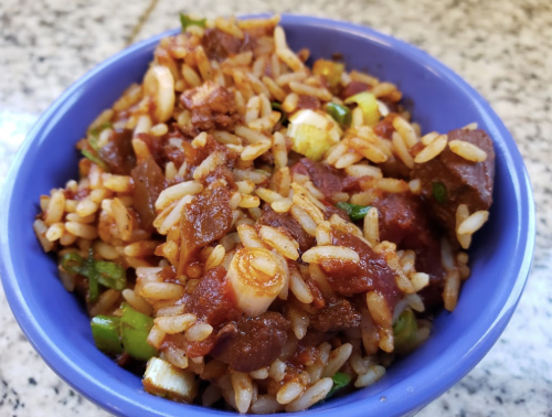 A blue bowl filled with rice mixed with meat, vegetables, and a rich sauce, placed on a speckled countertop.