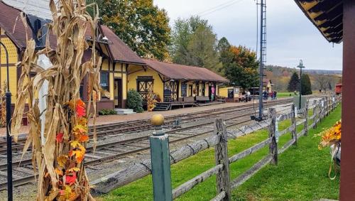 A quaint train station surrounded by autumn foliage and wooden fences, with tracks leading into the distance.