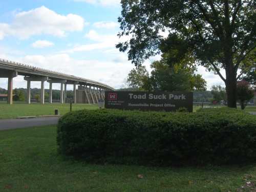 Sign for Toad Suck Park with a highway overpass in the background and green grass in the foreground.