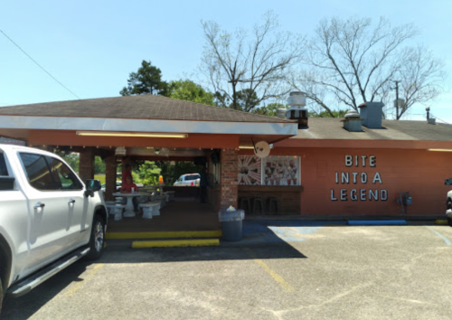 A restaurant with a sign reading "Bite Into a Legend," featuring outdoor seating and a parking area.