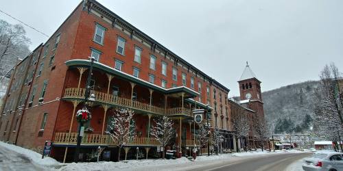 Historic brick buildings with snow-covered trees, a clock tower, and festive decorations on a winter street.