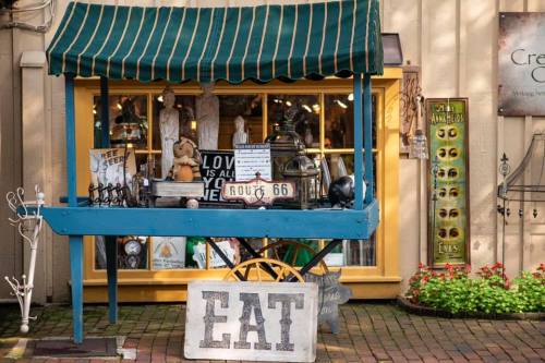 A charming outdoor market stall with vintage decor, signs, and a "EAT" sign in front of a colorful shop window.