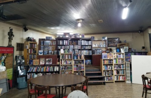 A cozy room filled with shelves of board games and books, featuring a round table and warm lighting.