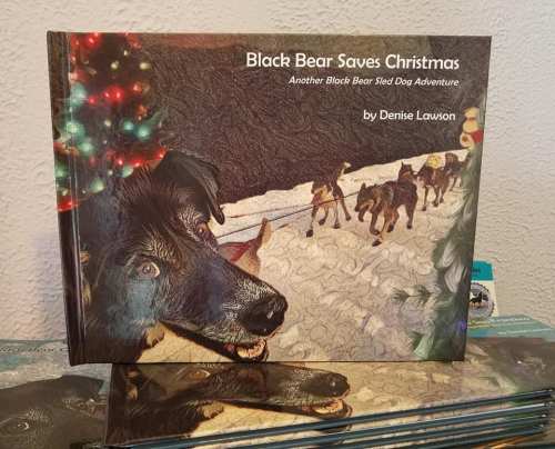 A children's book titled "Black Bear Saves Christmas" featuring a dog and a snowy scene, stacked on a table.