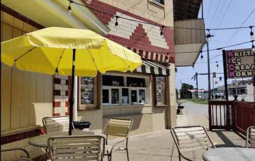 A bright yellow umbrella shades outdoor seating near an ice cream shop with a colorful sign.