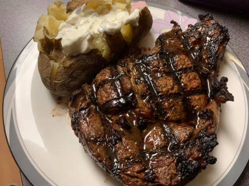 A grilled steak with a crosshatch pattern, served alongside a baked potato topped with sour cream.