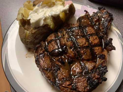 A grilled steak with a crosshatch pattern, served alongside a baked potato topped with sour cream.