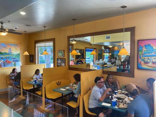 A busy restaurant interior with diners at booths, colorful decor, and a large mirror reflecting the space.