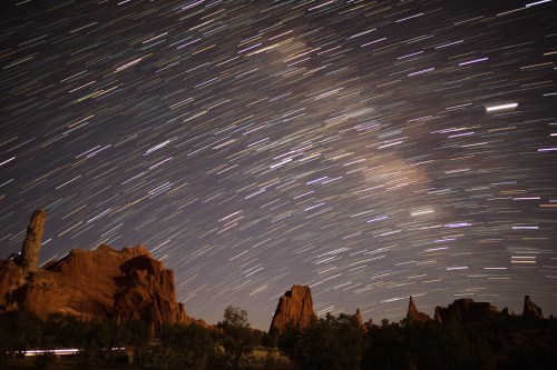 Star trails illuminate a night sky over red rock formations, creating a stunning celestial landscape.
