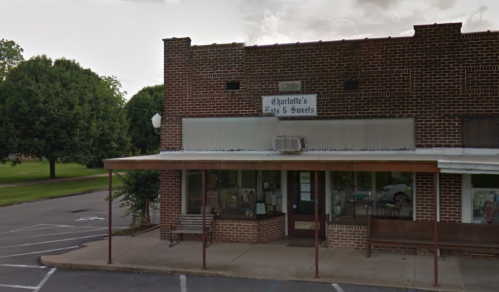 A brick building with a sign reading "Charlotte's Eats & Sweets," featuring a covered porch and parking area.