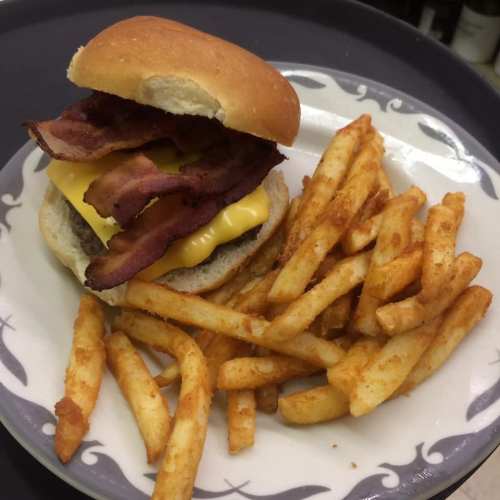 A cheeseburger with bacon on a bun, served with a side of golden, crispy French fries on a decorative plate.