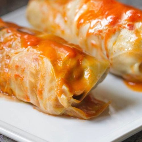 Two stuffed cabbage rolls drizzled with a rich tomato sauce on a white plate.