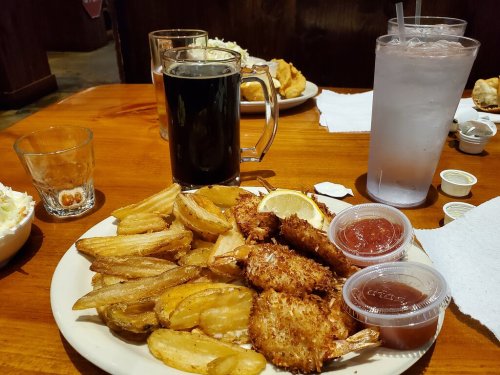 A plate of fried shrimp and golden fries, accompanied by dipping sauces, a glass of dark beer, and a glass of water.