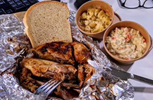 A meal featuring roasted chicken, macaroni and cheese, coleslaw, and a slice of bread, all served in takeout containers.