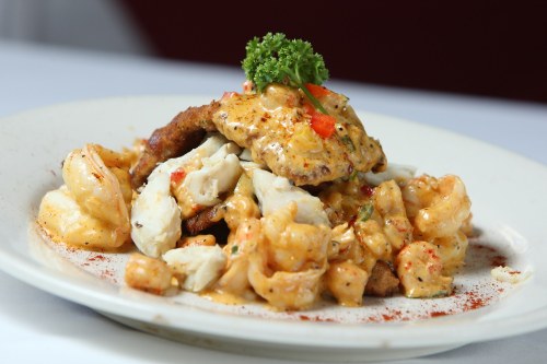A plate of seafood featuring shrimp, crab, and a fried fish fillet, topped with a creamy sauce and garnished with parsley.