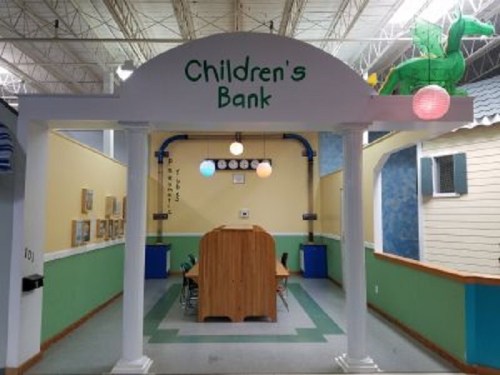 A colorful children's bank play area with a sign, tables, and playful decor in a bright, spacious room.