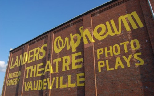 A brick wall featuring a large, vintage sign for the Landers Orpheum Theatre, advertising musical comedy and vaudeville.