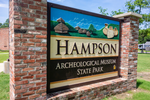 Sign for Hampson Archaeological Museum State Park, featuring a brick border and images of ancient structures and pottery.