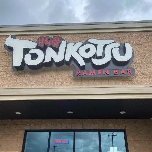 Sign for "Tonkotsu Ramen Bar" displayed on a brick building, with "Open" sign visible below.
